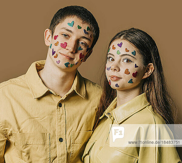 Smiling teenage couple with heart shape stickers on face in front of wall
