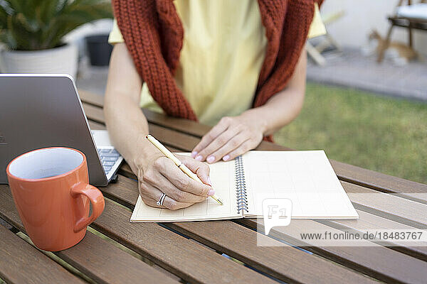 Hands of freelancer writing notes on table in garden