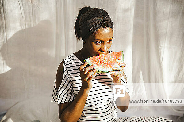 Nachdenkliche schwangere Frau isst frische Wassermelone im Hinterhof