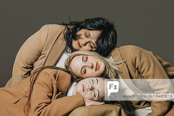 Teenage girl with woman and mother leaning head on each other against gray background