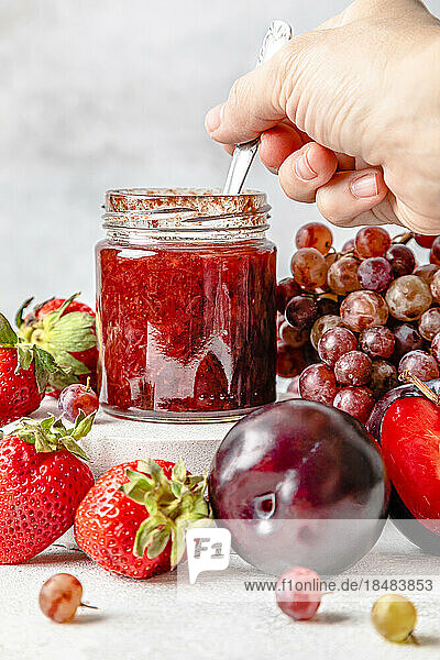Hand of woman holding spoon with homemade strawberry jam on table