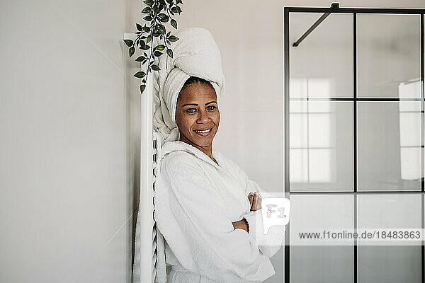 Smiling mature woman standing with arms crossed in bathroom at home
