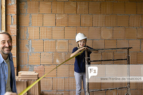 Happy girl measuring with tape measure in front of brick wall