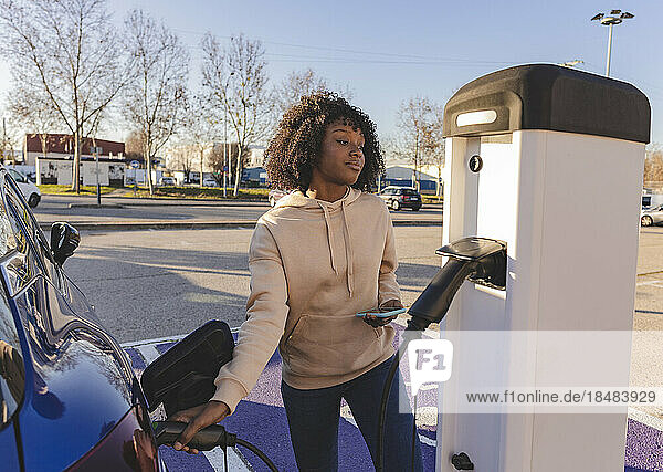 Young woman charging electric car at station