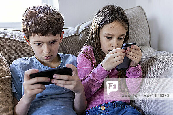 Mädchen und Junge benutzen Smartphone zu Hause auf dem Sofa