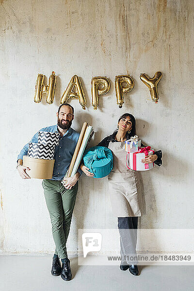 Smiling couple holding gift boxes leaning on wall