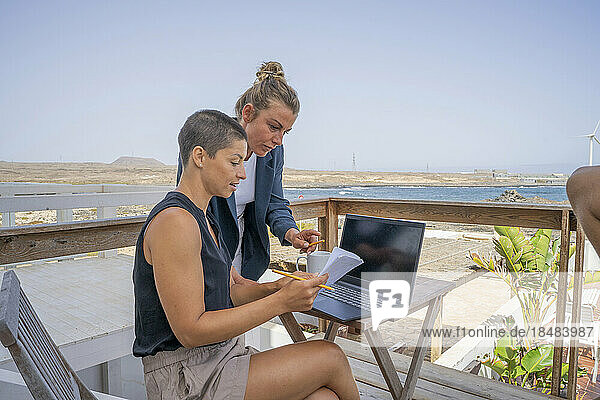 Businesswoman assisting colleague holding book on balcony