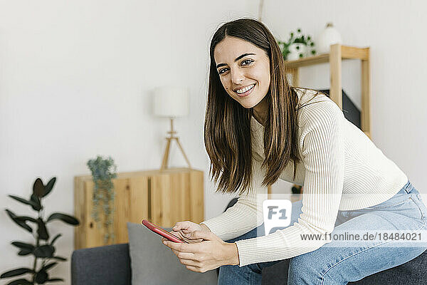 Smiling young woman sitting with smart phone at home