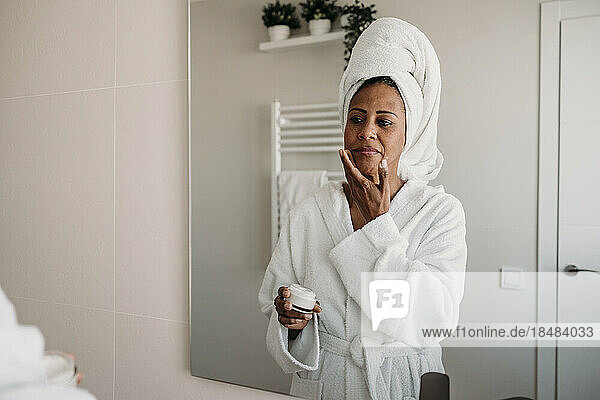 Mature woman applying moisturizer on face in bathroom