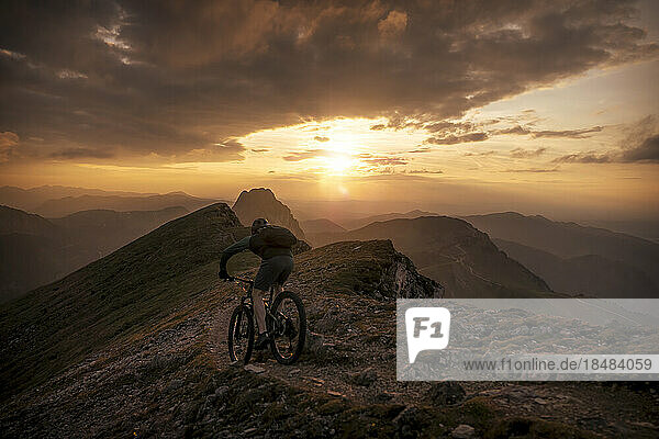 Man riding mountain bike on trail at sunset
