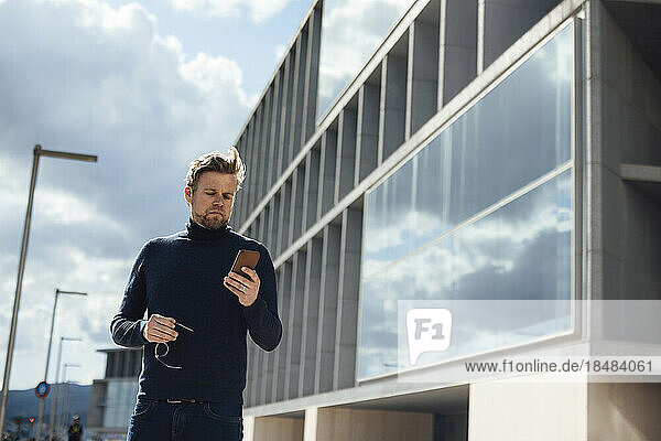 Businessman with eyeglasses using mobile phone by office building