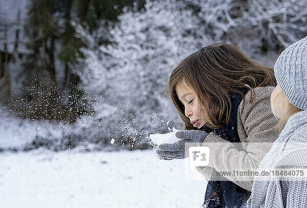 Cute girl blowing snow on hand by sister