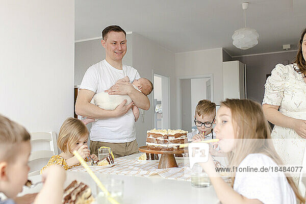 Father carrying son with children eating cake sitting at table