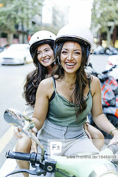Happy woman with friend sitting on electric scooter