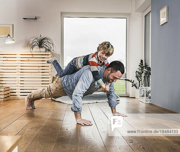 Happy boy balancing on back of father doing push-ups at home