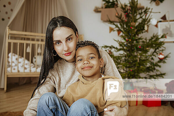 Smiling mother and son sitting in front of Christmas tree at home