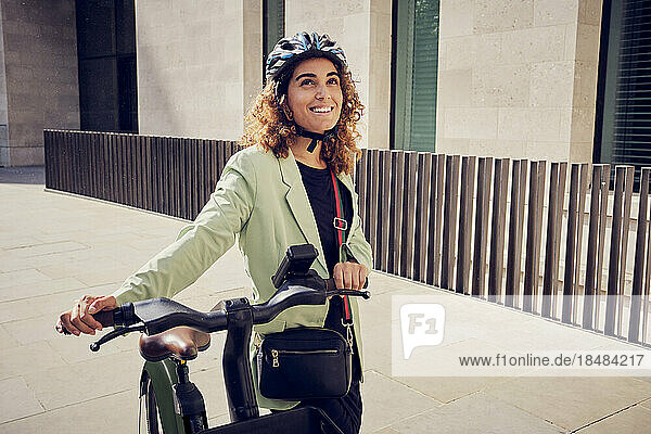Smiling businesswoman holding electric bicycle on footpath