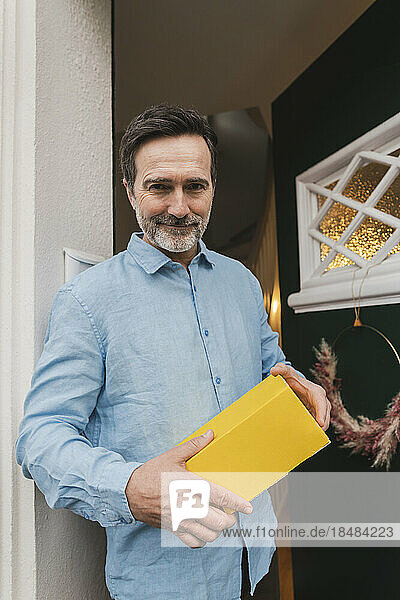 Mature man holding package standing at doorway