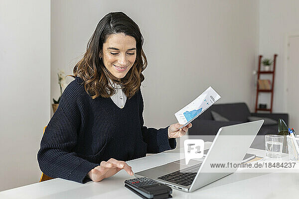 Businesswoman with document using calculator at desk