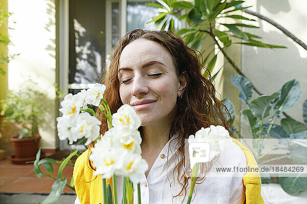 Smiling woman with eyes closed holding daffodil flowers in backyard