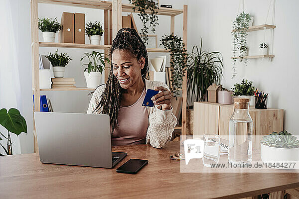 Lächelnder Freiberufler  der im Heimbüro mit Kreditkarte am Laptop bezahlt