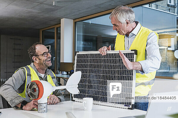 Engineer with solar panel discussing with colleague sitting at office