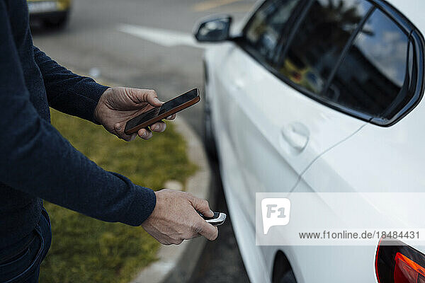 Man with mobile phone locking car with key