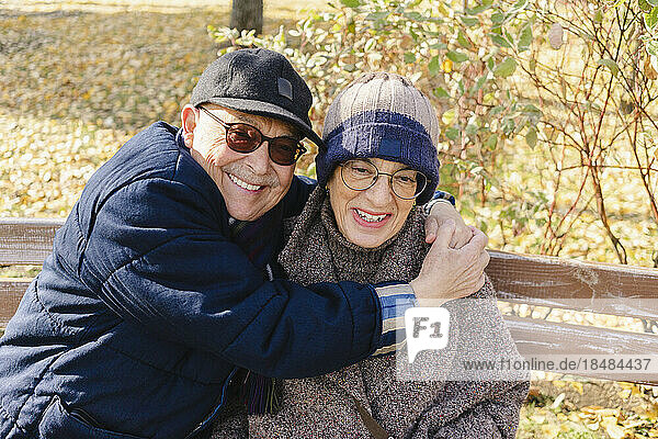 Happy senior man embracing woman sitting on bench