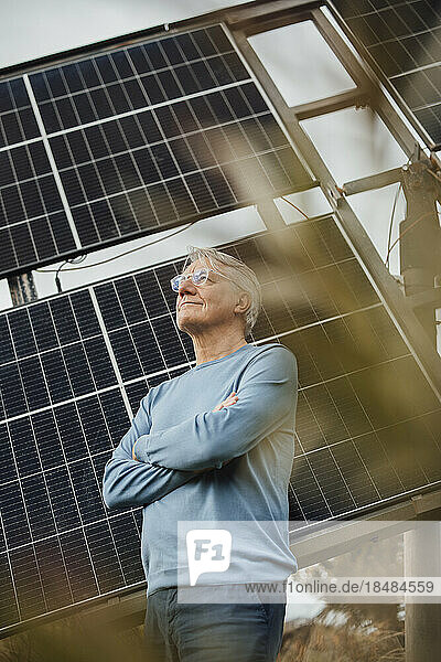 Smiling man standing with arms crossed standing by solar panels