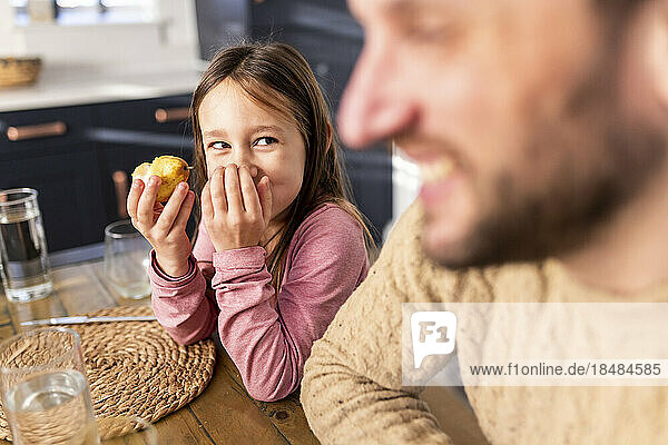 Happy girl having breakfast with father sitting at table