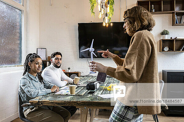 Geschäftsfrau zeigt Kollegen im Büro das Modell einer Windkraftanlage