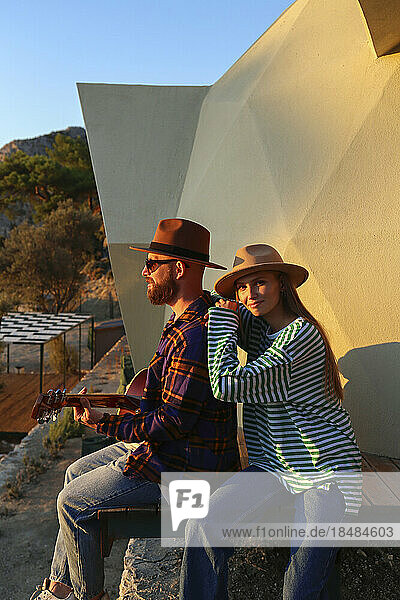 Hipster couple sitting together near eco home at sunset