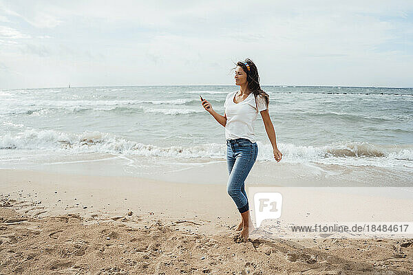 Frau läuft mit Smartphone auf Sand am Strand