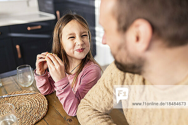 Smiling girl having breakfast with father sitting at table
