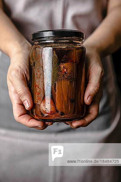 Hands of mature woman holding homemade pickled eggplant jar