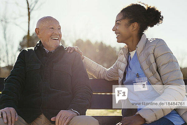 Happy senior man sitting with caretaker in park on sunny day