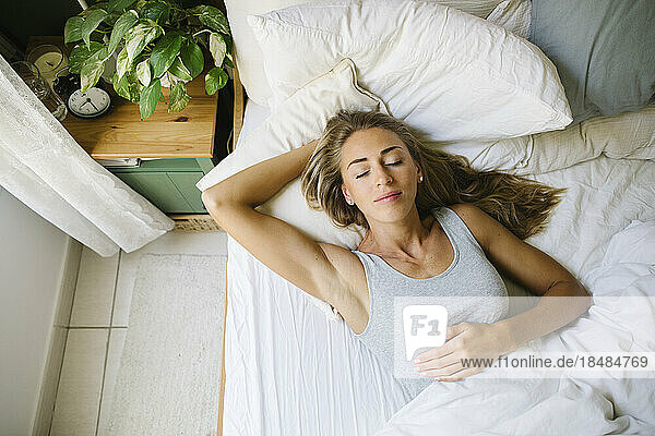 Woman with eyes closed resting in bed at bedroom