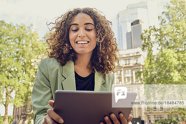 Smiling businesswoman with curly hair doing video call on tablet PC