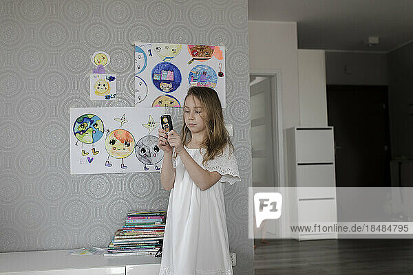 Mädchen spielt mit altem Telefon und steht zu Hause neben Zeichnungen an der Wand