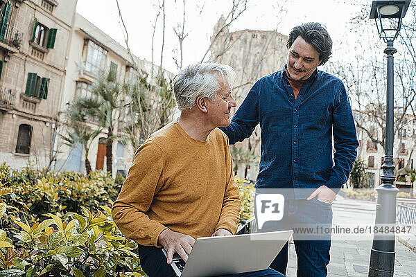 Smiling son with father holding laptop sitting by plants