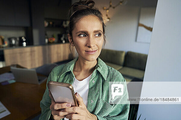 Thoughtful woman with mobile phone at home office