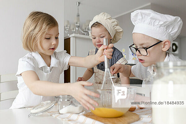 Mädchen mit Brüdern  die in der Küche Eier in einer Schüssel mischen