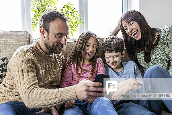 Cheerful family using smart phone on sofa in living room