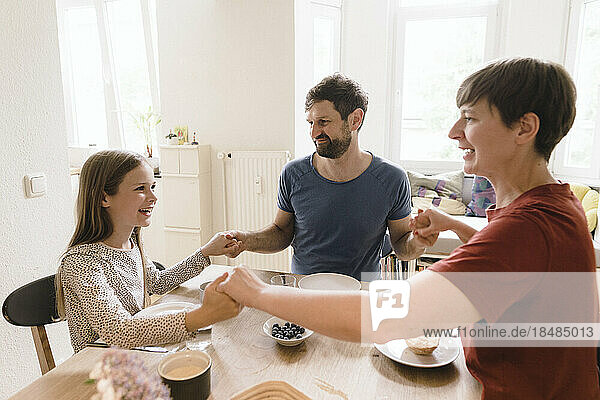 Family holding hands with each other sitting at dining table in home
