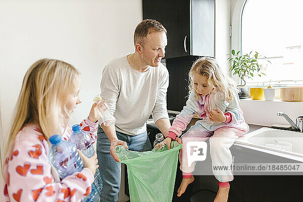 Smiling father recycling plastic bottles with daughters at home