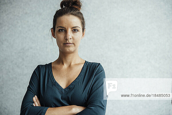 Confident businesswoman standing with arms crossed in front of wall