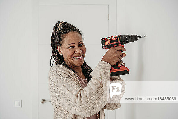 Happy woman using drill machine on wall at home