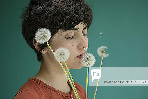 Young woman smelling dandelions against green background