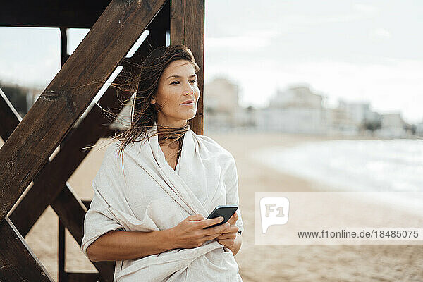 Frau mit Smartphone lehnt an Rettungsschwimmerhütte am Strand