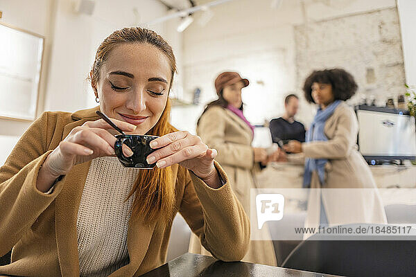 Smiling woman holding coffee cup with friends standing in background